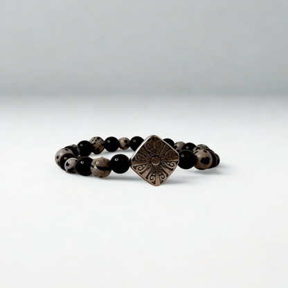 Black beaded bracelet with a bronze square pendant on a white background