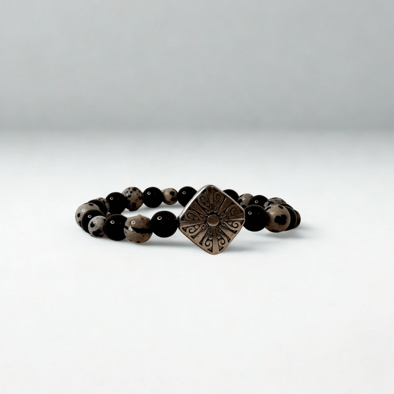Black beaded bracelet with a bronze square pendant on a white background